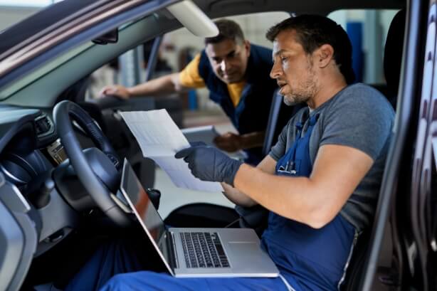 Automechaniker mit Laptop und Papieren in einem Fahrzeug